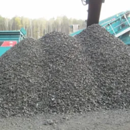 Góra węgla kamiennego o frakcji groszku, usypana na placu składowym, z widocznymi przesiewaczami i sortownikami w tle.