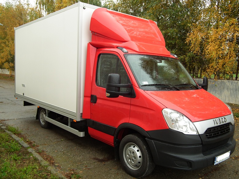 Czerwony samochód dostawczy Iveco z białą zabudową kontenerową, zaparkowany na zewnątrz, widok z przodu.