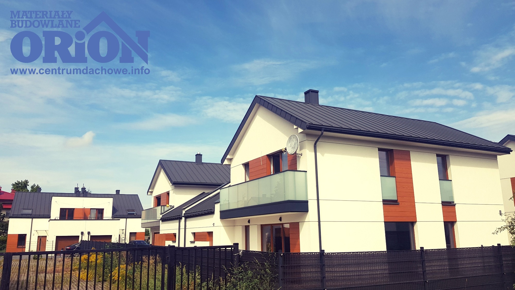 Nowoczesne domy jednorodzinne z ciemnymi, metalowymi dachami i jasną elewacją, widoczne zza ogrodzenia, logo firmy na górze kadru.