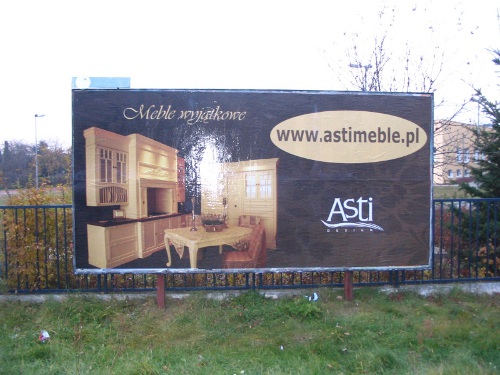 Billboard z reklamą mebli kuchennych i jadalnianych firmy Asti, widoczny adres strony internetowej www.astimeble.pl, na tle zieleni miejskiej.