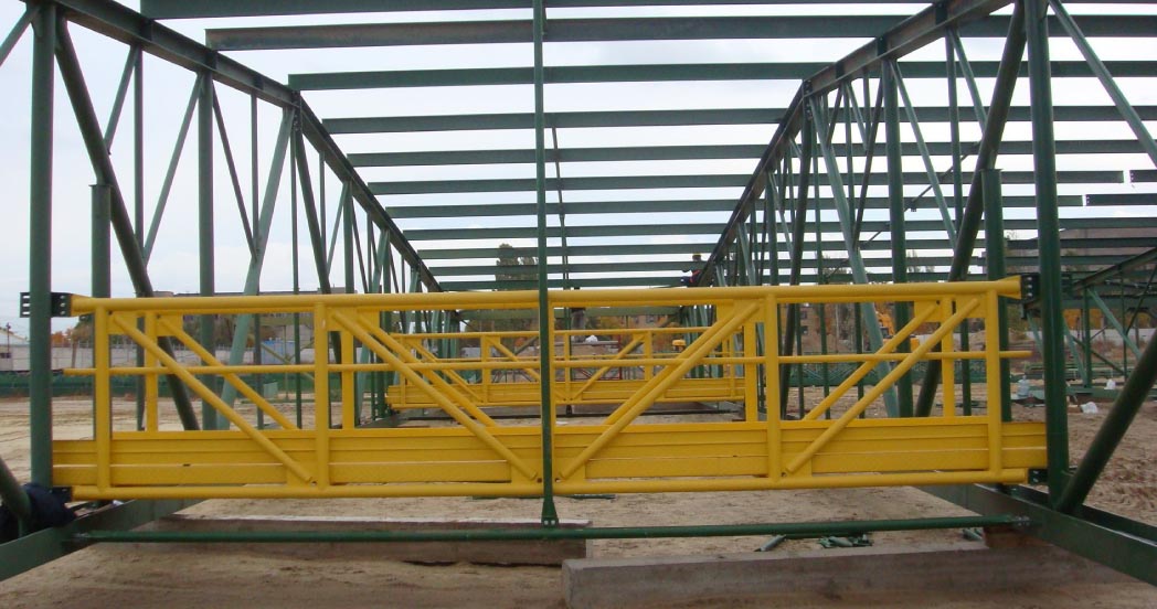 Żółta, stalowa konstrukcja pomostu roboczego zawieszona na zielonej konstrukcji szkieletowej budynku w trakcie budowy.