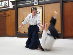 Mężczyzna w białym kimonie wykonuje rzut na partnerze podczas treningu sztuk walki w Zabrzu. Widoczny dynamiczny ruch i skupienie na technice.