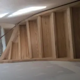 Surowe, jasne drewniane stopnie schodów w trakcie montażu, widoczne elementy konstrukcyjne i zabezpieczenia, tło stanowi surowy stan wykończenia wnętrza.