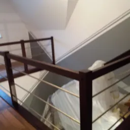 Nowoczesna balustrada z ciemnego drewna i metalowych prętów, widok z góry na schody w trakcie remontu, zabezpieczone folią malarską.