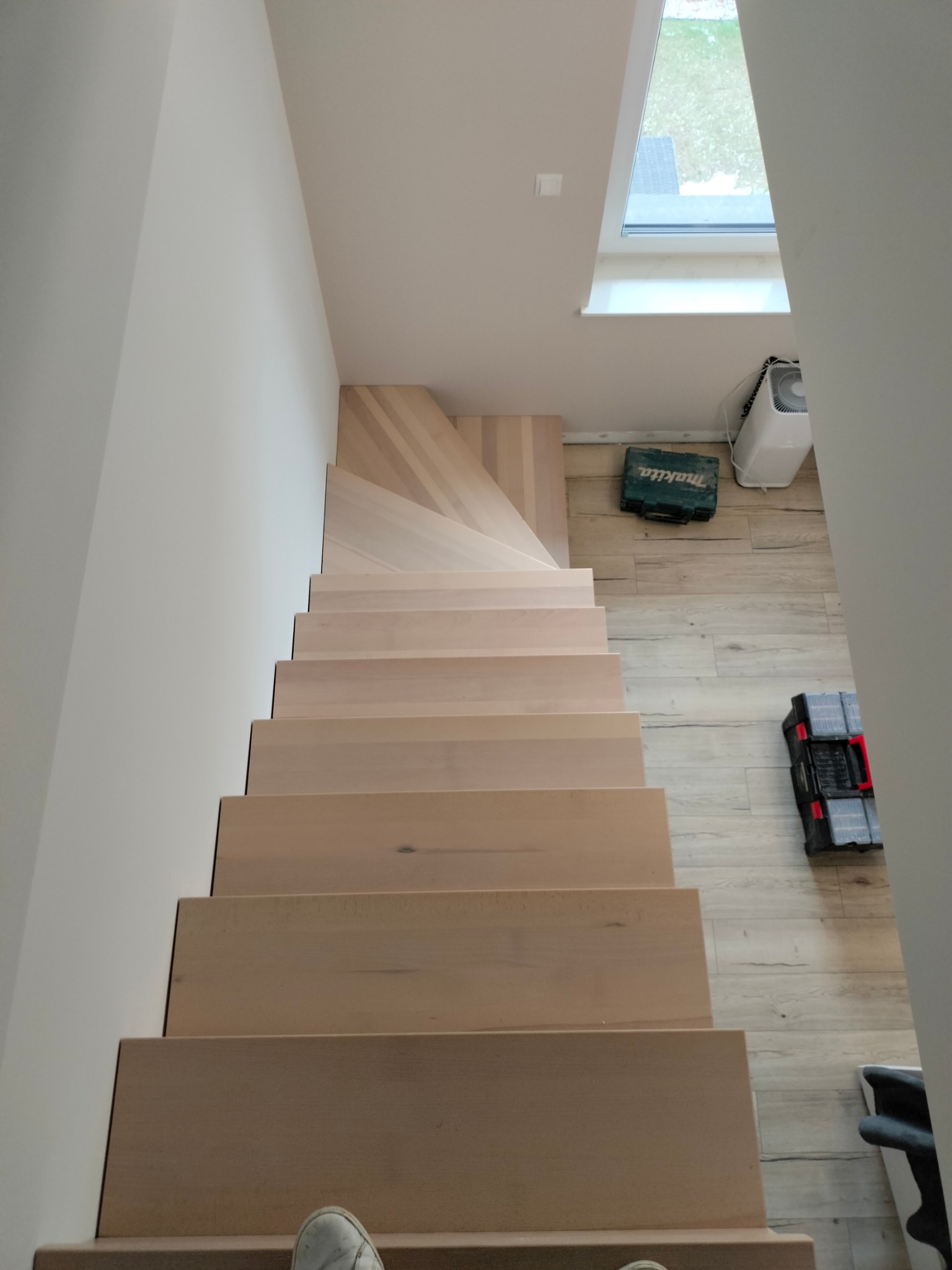 Nowoczesne, jasne schody z drewna, widziane z góry. Minimalistyczny design, skrzynki narzędziowe na podłodze, naturalne światło z okna dachowego.