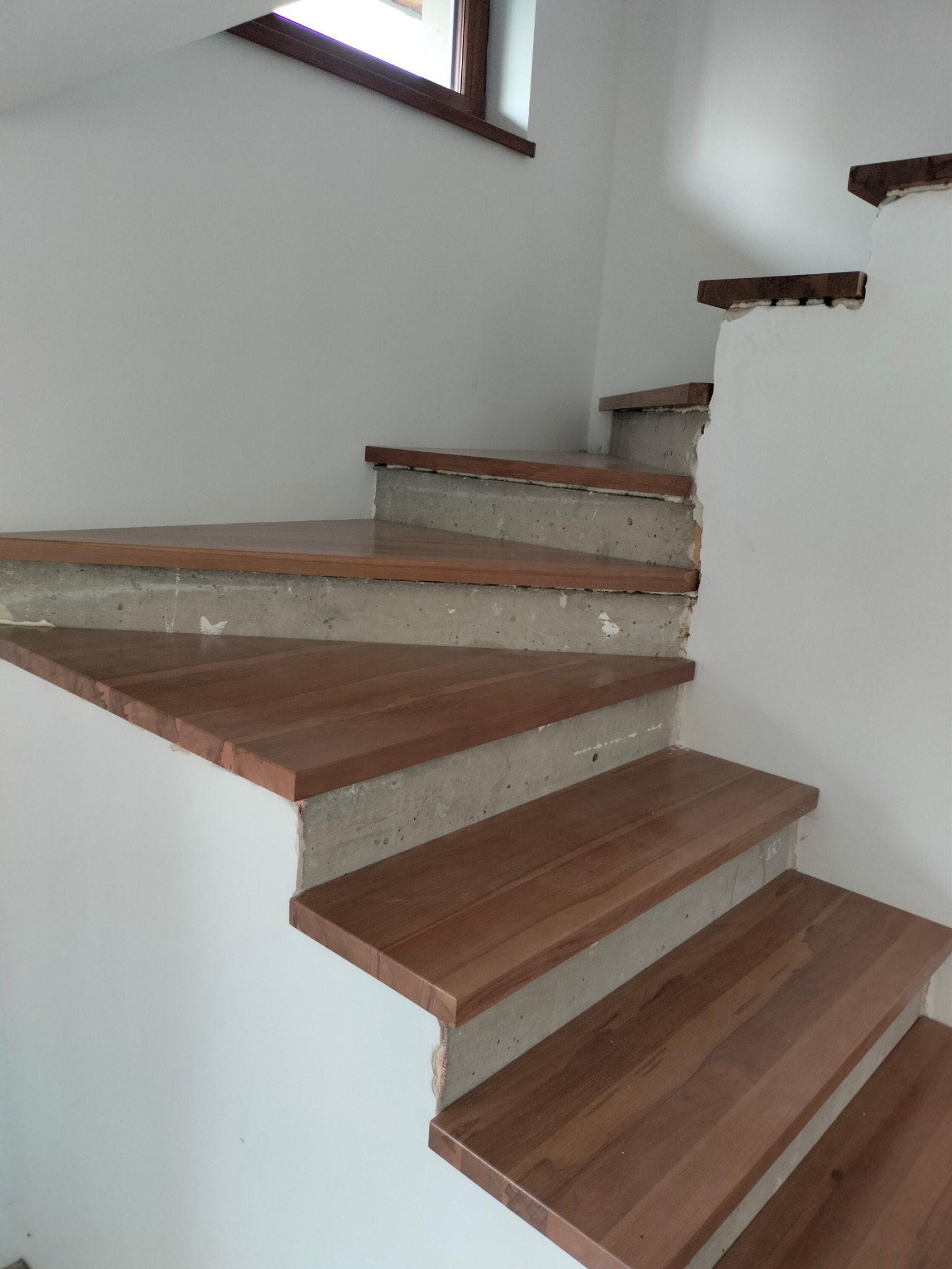 Wewnętrzne schody z drewnianymi stopniami w trakcie montażu. Widoczne betonowe podesty i fragment ściany. Ujęcie z dołu, podkreślające etap prac wykończeniowych.