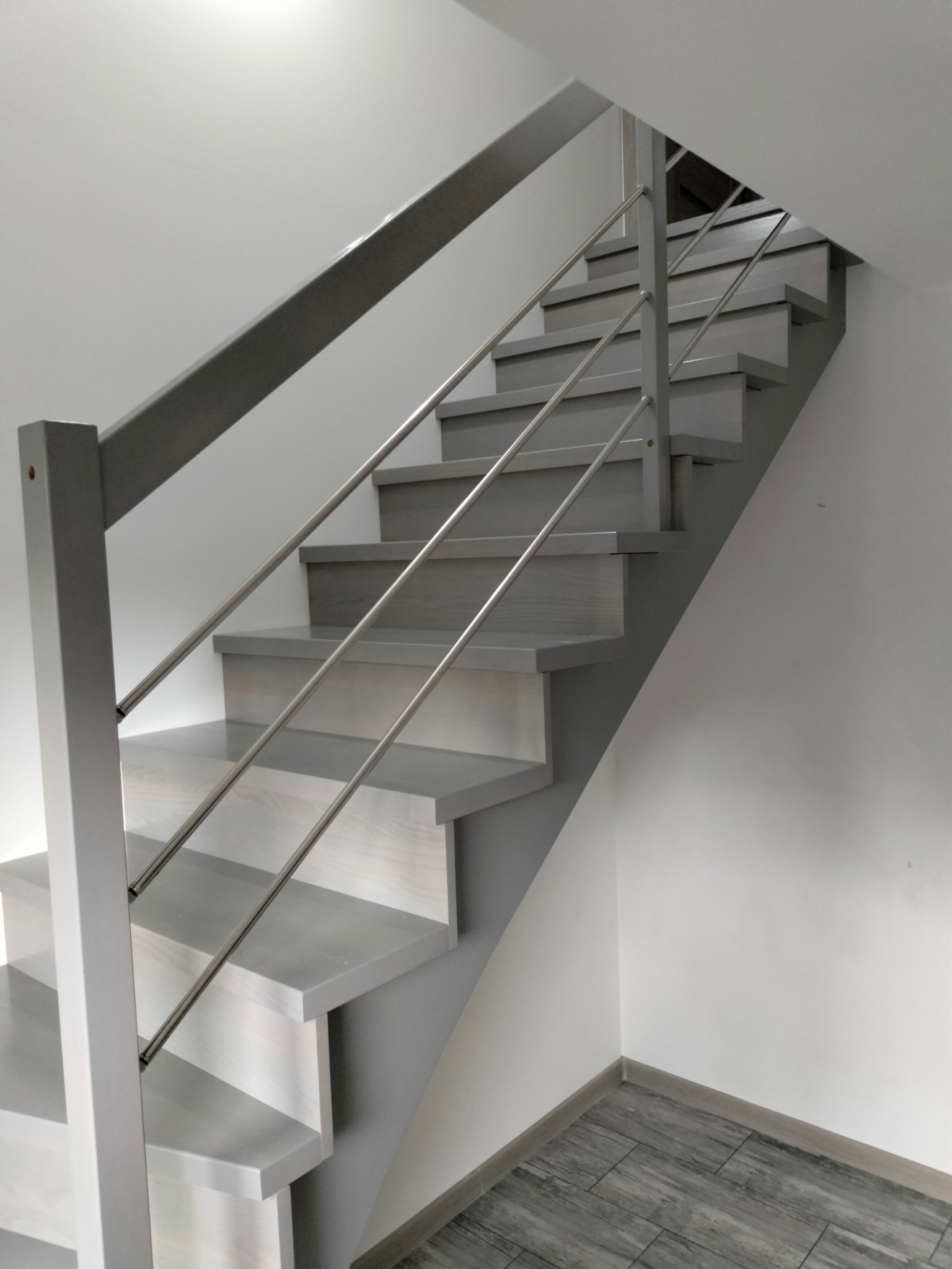 Nowoczesne, szare schody z metalową balustradą w minimalistycznym wnętrzu. Widoczne detale wykończenia i subtelna gra światła. Ujęcie z dołu w kierunku góry.