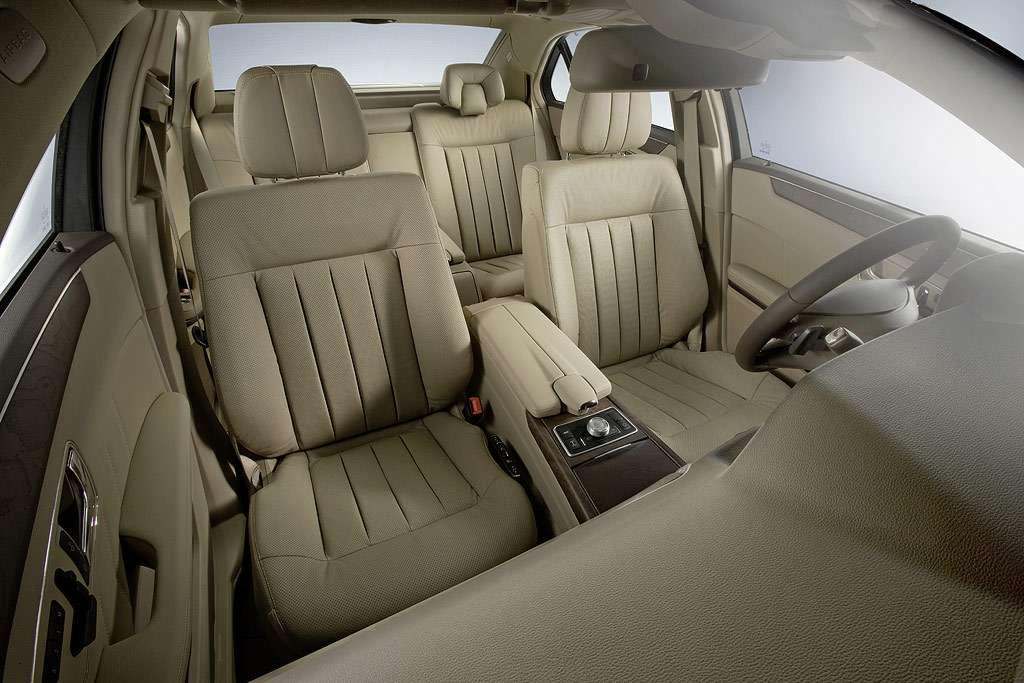 Beżowe skórzane wnętrze luksusowego samochodu z widocznymi fotelami, deską rozdzielczą i kierownicą. Detale wykończenia z elementami drewnianymi.