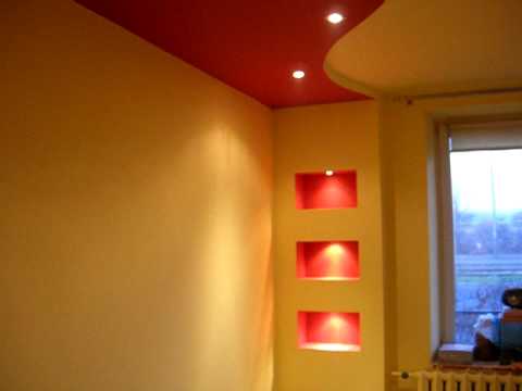 Żółte ściany z trzema wnękami podświetlonymi na czerwono, czerwony sufit z wbudowanymi punktowymi lampami, widok na okno z grzejnikiem pod spodem.