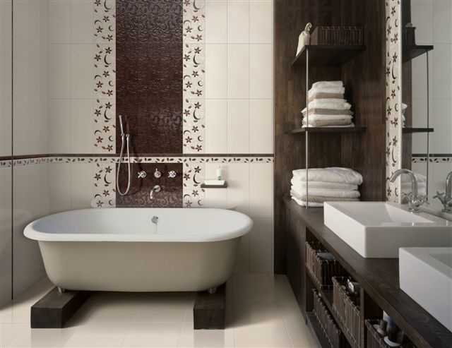 Elegancka łazienka z wolnostojącą wanną na ciemnych, drewnianych podkładkach, ozdobnymi płytkami ściennymi w odcieniach brązu i beżu oraz drewnianą zabudową z półkami i wiklinowymi koszami.