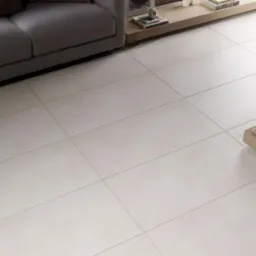 Jasnobeżowe, matowe płytki podłogowe 45x90 ułożone w salonie, widoczny narożnik szarej sofy i stolik kawowy z dekoracjami.