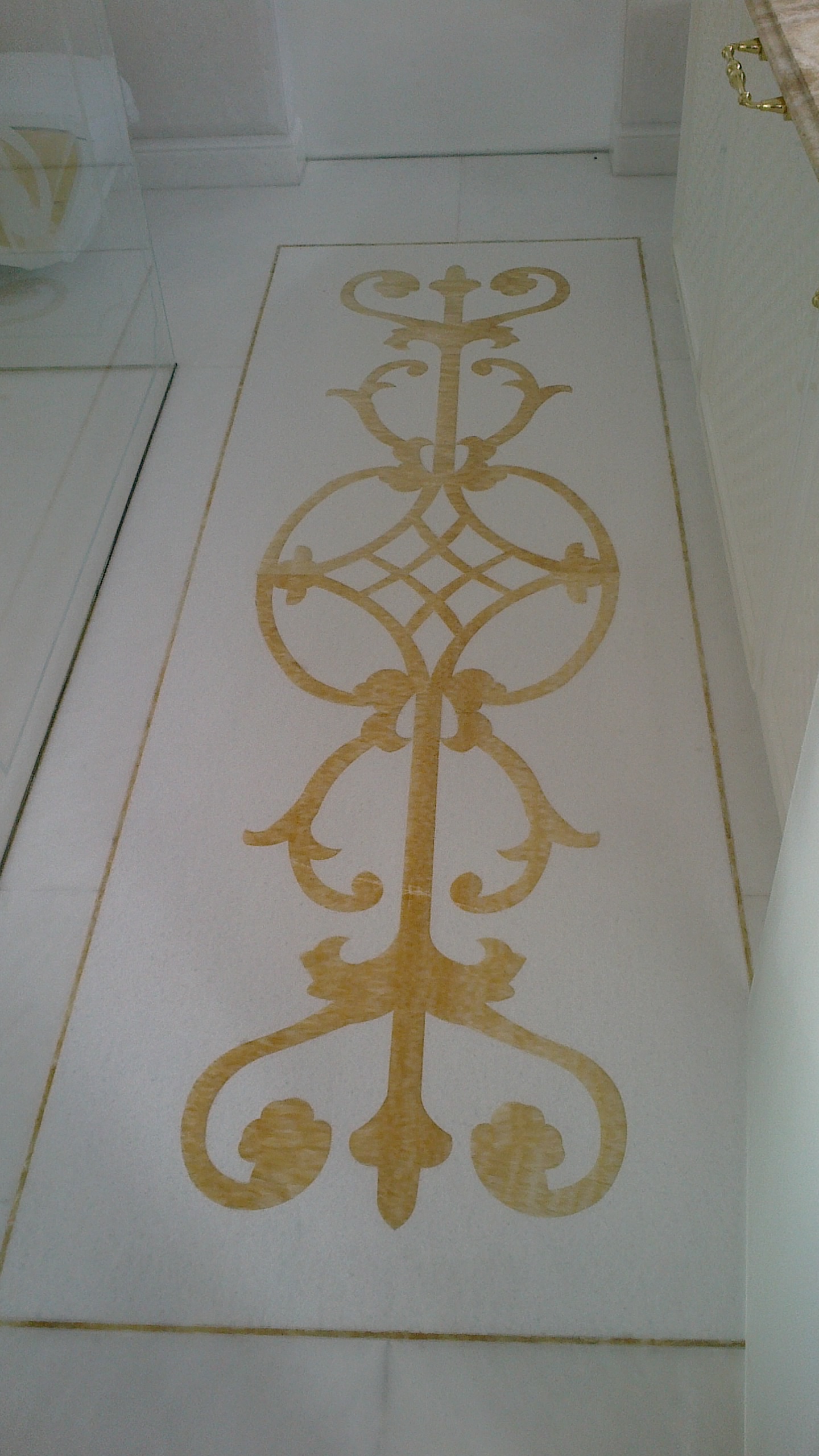 Polerowany blat kamienny z wzorem ornamentacyjnym w odcieniach beżu, wkomponowany w wystrój wnętrza, widoczny fragment szafki z uchwytem.