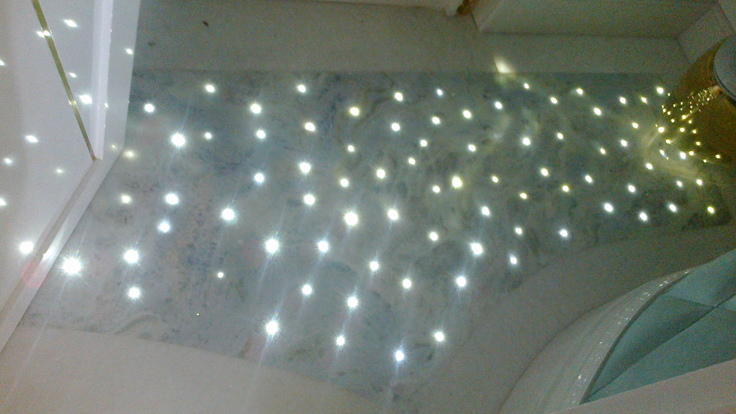 Podświetlany blat z kamienia naturalnego z równomiernie rozmieszczonymi punktami świetlnymi, widoczne fragmenty wykończenia wnętrza.