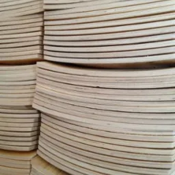 Stosy jasnej, surowej tarcicy ułożone w równych warstwach, widoczne krawędzie desek z wyraźnym usłojeniem.