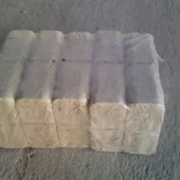 Zwarta paczka sprasowanego materiału opałowego, owinięta folią, leżąca na betonowej powierzchni.