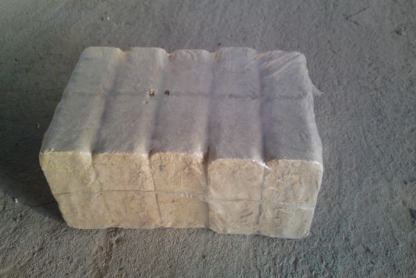 Zwarta paczka sprasowanego materiału opałowego, owinięta folią, leżąca na betonowej powierzchni.