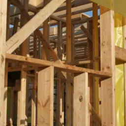 Konstrukcja szkieletowa domu jednorodzinnego w Halinowie, widoczne drewniane belki i słupy, częściowo zabezpieczone żółtą folią izolacyjną.