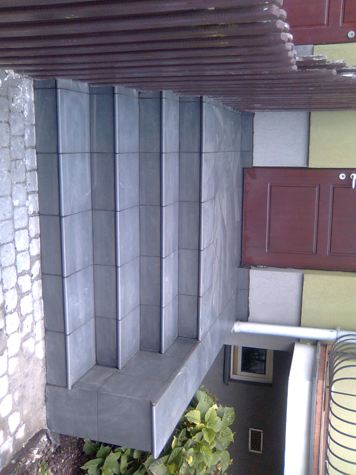 Schody wejściowe wyłożone ciemną, grafitową terakotą, prowadzące do drzwi wejściowych. Widoczne detale wykończenia elewacji.