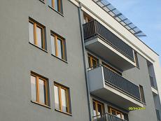 Elewacja budynku wielorodzinnego w szarym kolorze z drewnianymi ramami okiennymi i czarnymi balustradami balkonów, widok z dołu