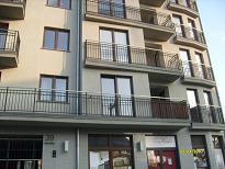 Wielopiętrowy budynek mieszkalny po remoncie elewacji, z nowymi oknami, balkonami z czarnymi, metalowymi balustradami i świeżo pomalowaną fasadą w odcieniach szarości.