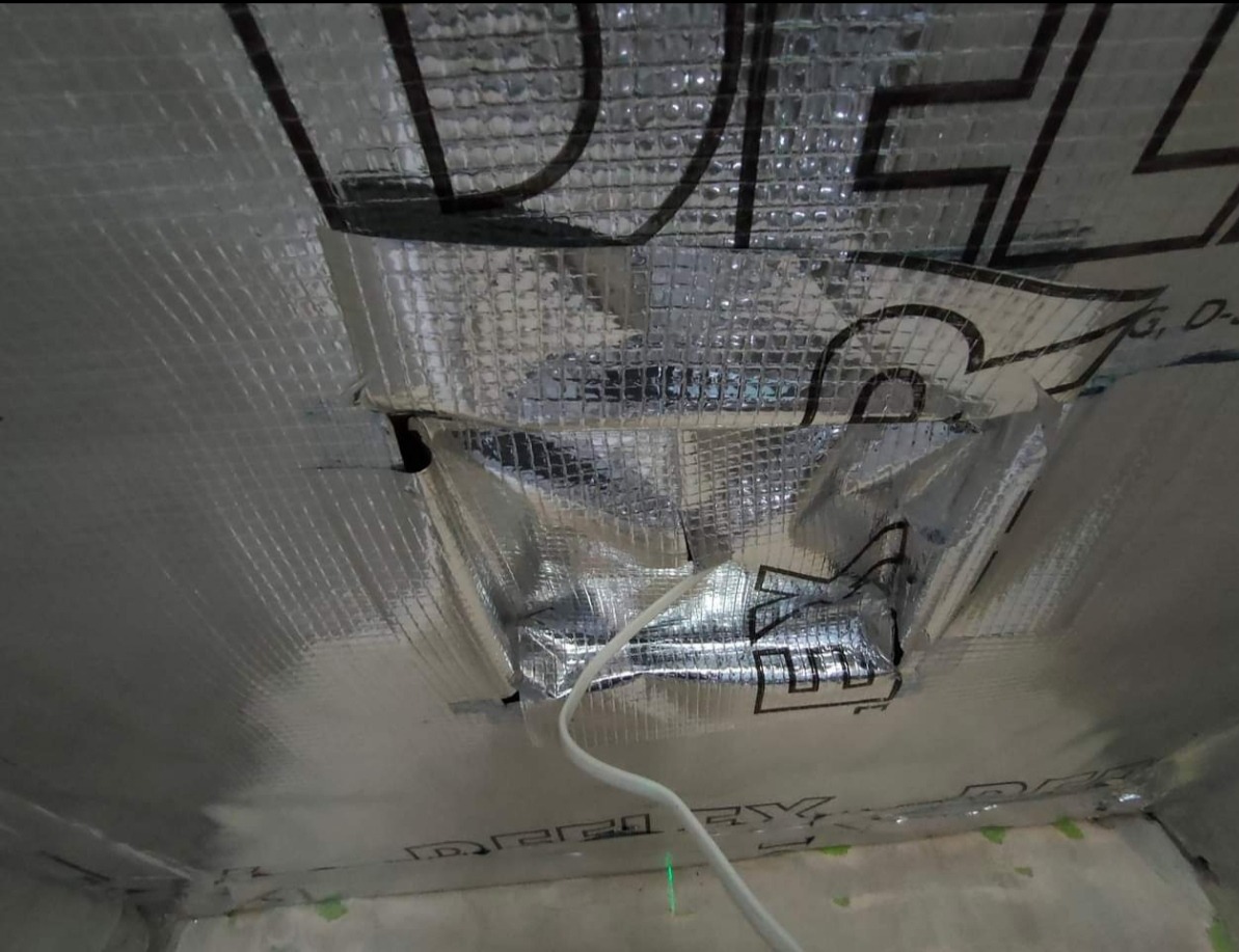 Izolacja termiczna sufitu z widocznym kablem elektrycznym, folia aluminiowa z nadrukiem, fragment ściany z zieloną linią lasera.
