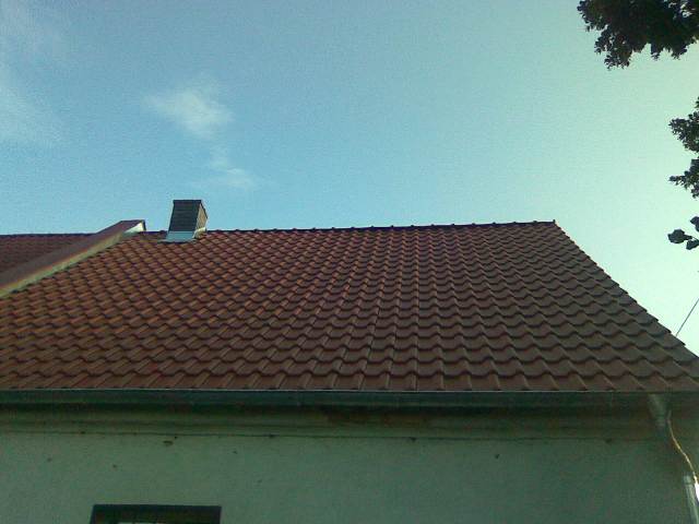 Czerwony dach z dachówki ceramicznej, widoczny komin i rynna, ujęcie z dołu w słoneczny dzień.