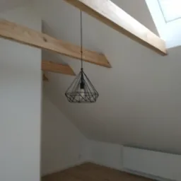 Poddasze po remoncie z drewnianymi belkami stropowymi, nowoczesną lampą wiszącą i oknem dachowym