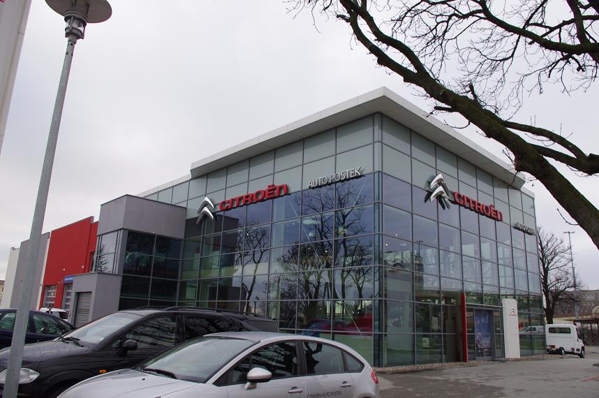 Nowoczesny budynek salonu samochodowego Citroen Auto Postek z przeszkloną fasadą, widoczne logo marki i zaparkowane samochody.