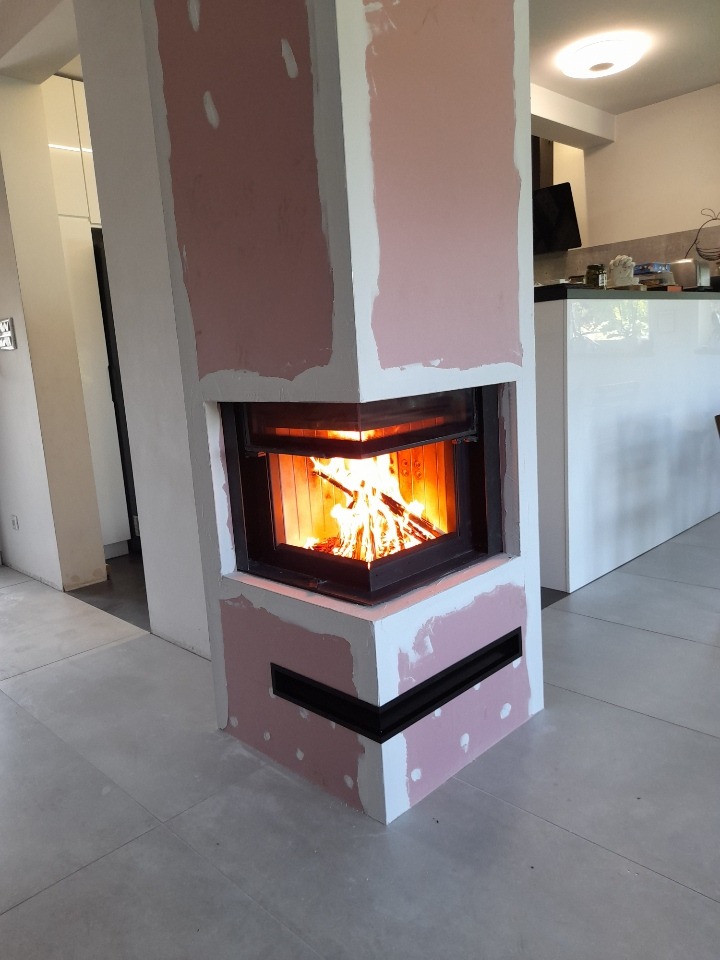 Wnętrze domu z widocznym kominkiem w trakcie obudowy, z palącym się drewnem wewnątrz, szpachlowane ściany, nowoczesny design.