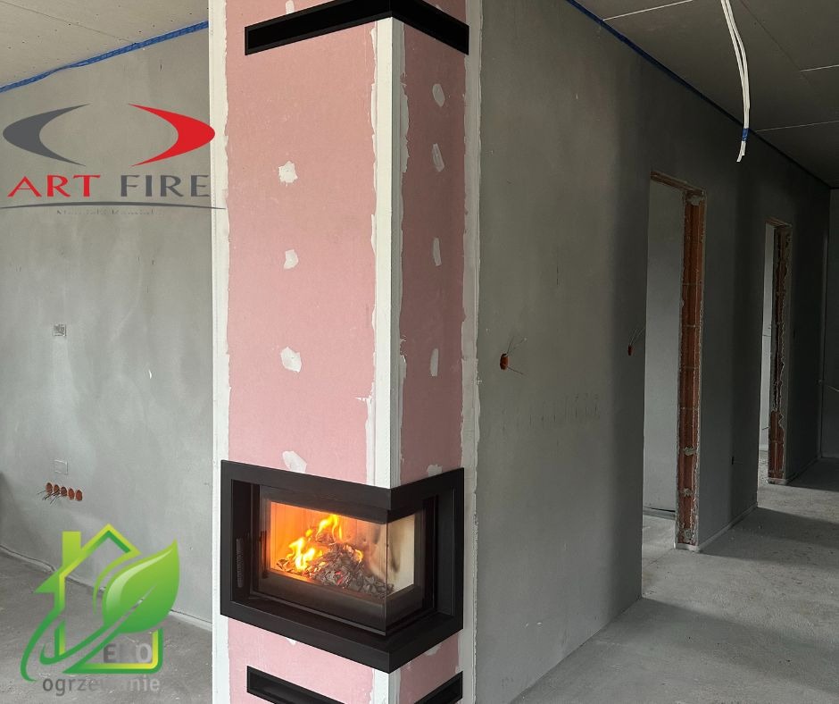 Wnętrze w trakcie wykończenia z narożnym wkładem kominkowym z czarną ramą, obudowanym płytami kartonowo-gipsowymi w kolorze różowym, widoczne płomienie wewnątrz paleniska, logo firmy Art Fire...