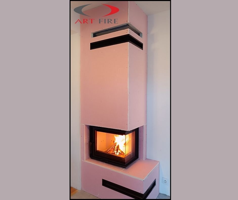 Wysoki kominek z obudową z płyt kartonowo-gipsowych w kolorze różowym, z widocznym paleniskiem i płomieniami, jeszcze przed ostatecznym wykończeniem.