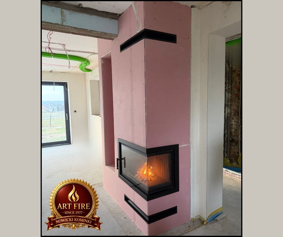 Narożny kominek obudowany płytami gipsowo-kartonowymi w trakcie montażu, widoczne elementy wentylacyjne i płomień w palenisku. Surowy stan wykończenia wnętrza.