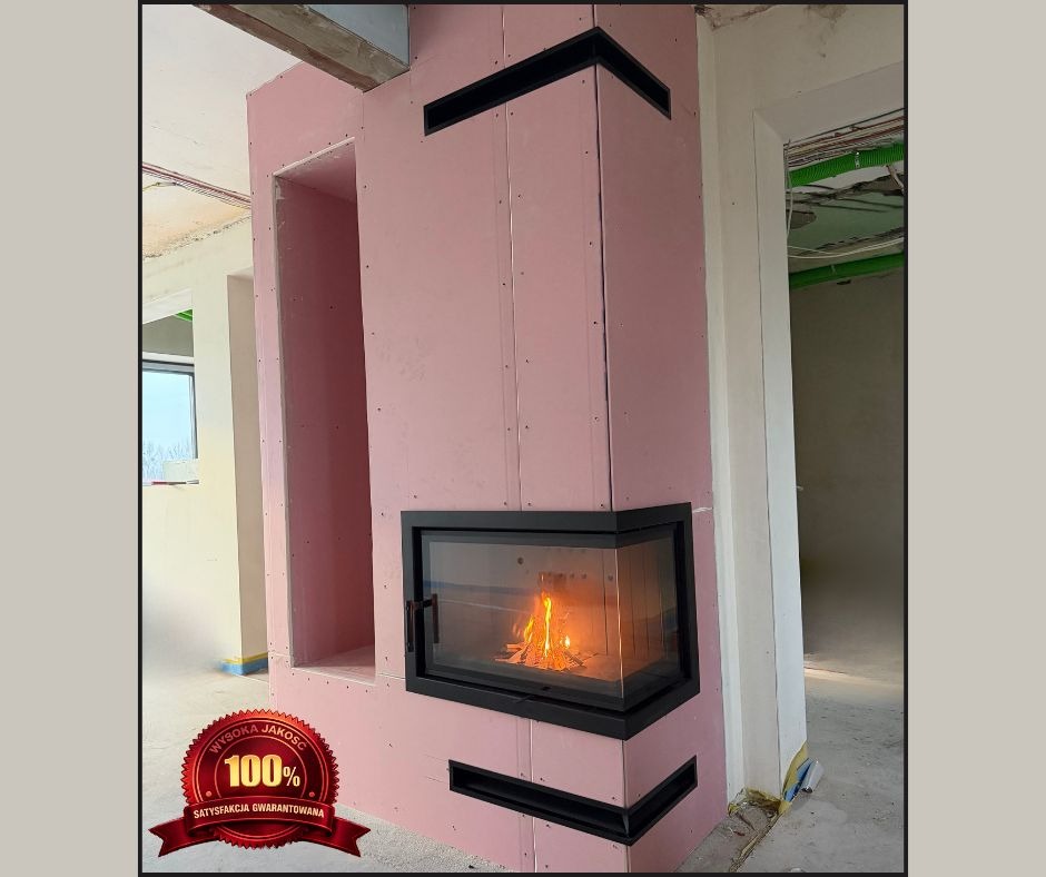 Narożny kominek z czarną ramą i paleniskiem w trakcie obudowy płytami gipsowymi, widoczne elementy wentylacyjne i fragment pomieszczenia w stanie surowym.