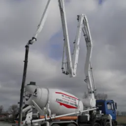 Ciężarówka z pompą do betonu z wysięgnikiem teleskopowym ustawiona na placu budowy, na zbiorniku widoczne logo firmy.
