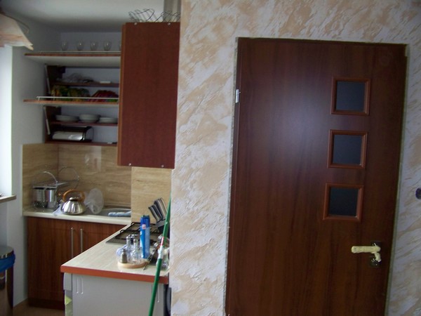 Wnętrze kuchni z brązowymi szafkami i drzwiami z trzema kwadratowymi okienkami, ściany wykończone dekoracyjnym tynkiem.