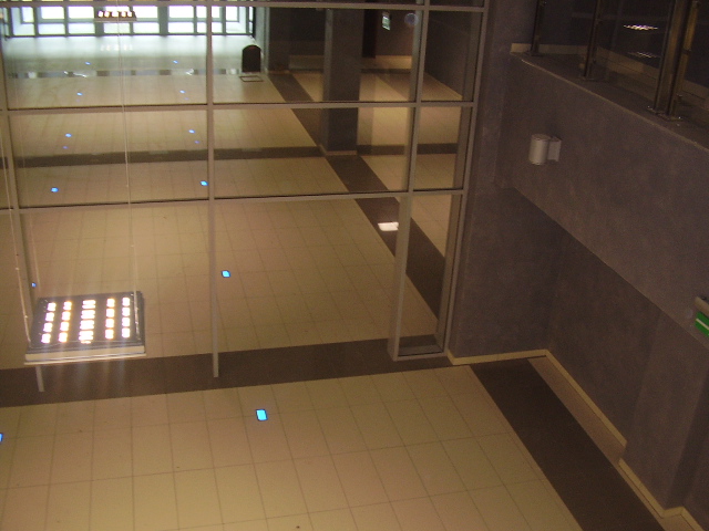 Wnętrze biura z podświetlaną podłogą, widok z góry przez szklaną ścianę.