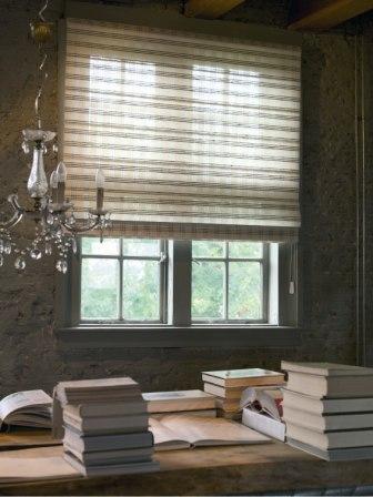 Zasłonięte okno z poziomymi paskami, widoczne zza sterty książek i kryształowego żyrandola w pokoju o kamiennych ścianach.