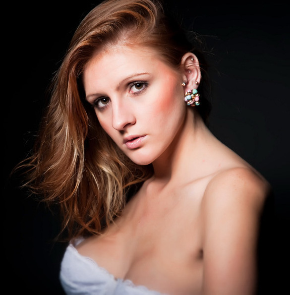 Portret modelki z Bielsko-Białej z rudymi włosami i delikatnym makijażem, noszącej ozdobne kolczyki na czarnym tle.