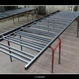 Instal-spaw usługi hydrauliczne i spawalnicze Sebastian Lewczuk - Metalowy szkielet ogrodzenia, spawane profile na kozłach. Widoczne spawy, surowy metal, przygotowanie do malowania. Kątowe ujęcie, warsztatowe tło.