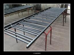 Metalowy szkielet ogrodzenia, spawane profile na kozłach. Widoczne spawy, surowy metal, przygotowanie do malowania. Kątowe ujęcie, warsztatowe tło.