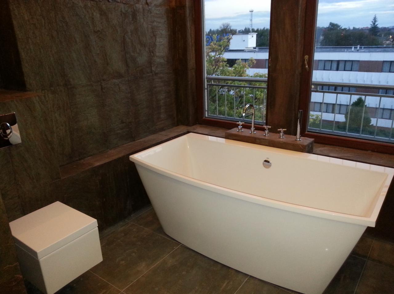 Nowoczesna, wolnostojąca wanna w łazience z kamienną okładziną w Poznaniu, widok na budynek zza okna.