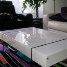 Biały, lakierowany stolik kawowy o minimalistycznym designie z czarnymi akcentami, ustawiony na wzorzystym dywanie w salonie z czarnym skórzanym fotelem i białą sofą w tle.