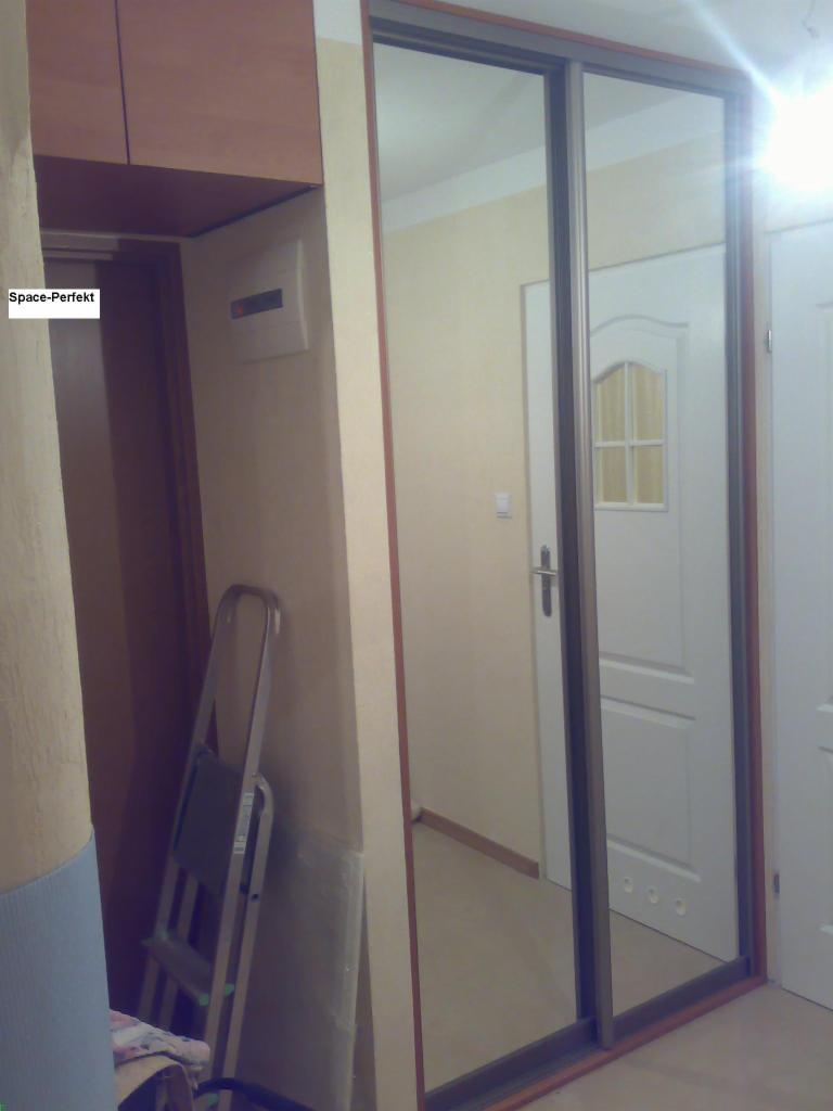 Wnętrze z szafą wnękową z lustrzanymi drzwiami przesuwnymi, widoczna drabina i częściowo zasłonięte wejście do pomieszczenia.