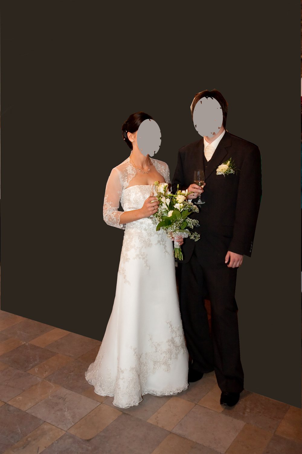 Para młoda w strojach ślubnych: panna młoda w białej sukni z koronkowymi aplikacjami i bolerku, trzyma bukiet, pan młody w czarnym garniturze z butonierką, oboje trzymają kieliszki z szampanem.