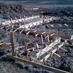 Przygotowanie szalunków pod fundamenty domu na grząskim terenie, widoczne drewniane konstrukcje i częściowo zalany beton.