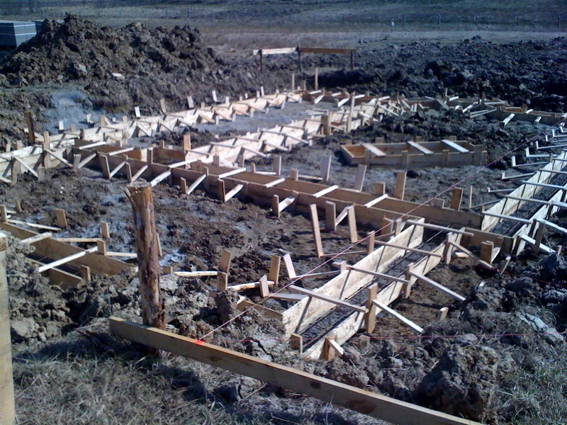 Przygotowanie szalunków pod fundamenty domu na grząskim terenie, widoczne drewniane konstrukcje i częściowo zalany beton.