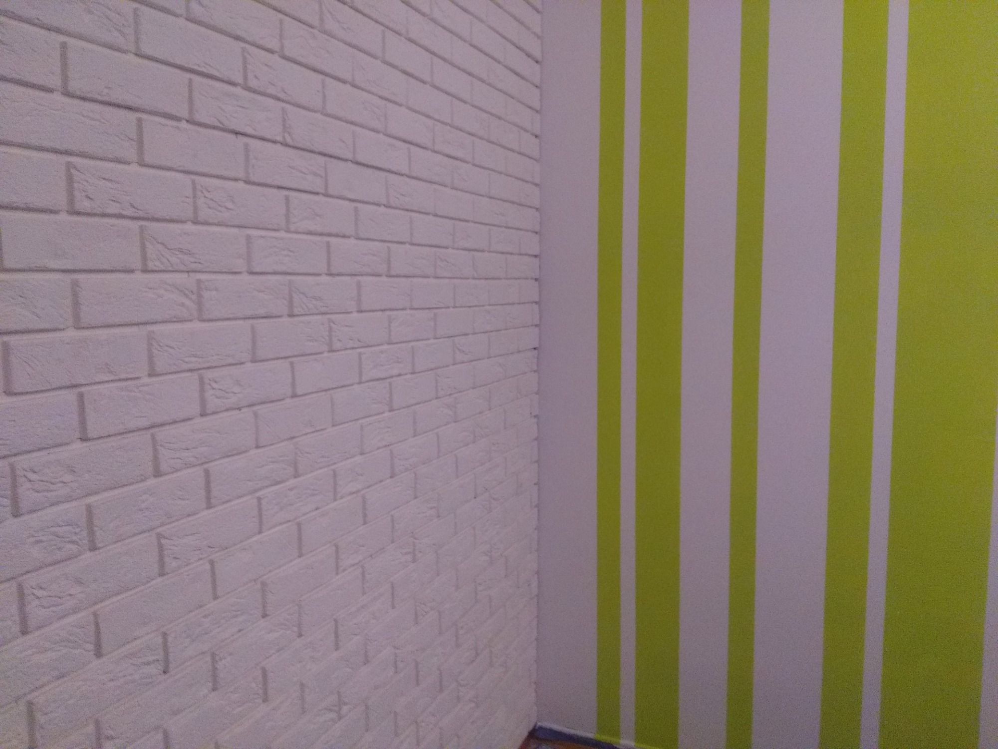 Wnętrze z białą ścianą z cegły dekoracyjnej i ścianą w pionowe, zielono-białe pasy.