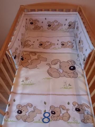 Łóżeczko dziecięce z pościelą dwuelementową w jasnych kolorach, wzór w pieski trzymające kości, widoczna numer 8 na kołderce.