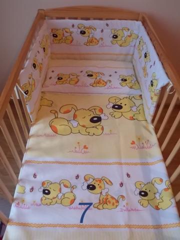 Komplet pościeli dziecięcej 3-elementowej z motywem żółtych piesków z kością, w drewnianym łóżeczku szczebelkowym, widoczny numer '7' na prześcieradle.