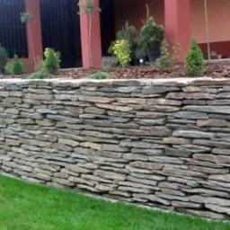 Kamienny murek oporowy z nasadzeniami roślin ozdobnych, widok z poziomu trawnika.